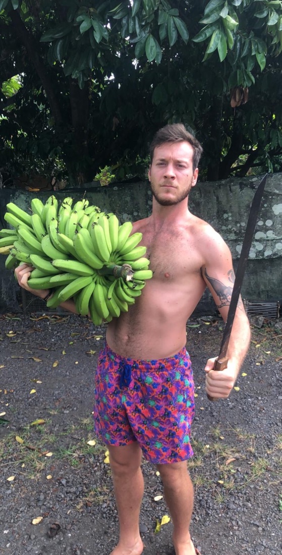 Steven in the wild, holding bananas and a machete
